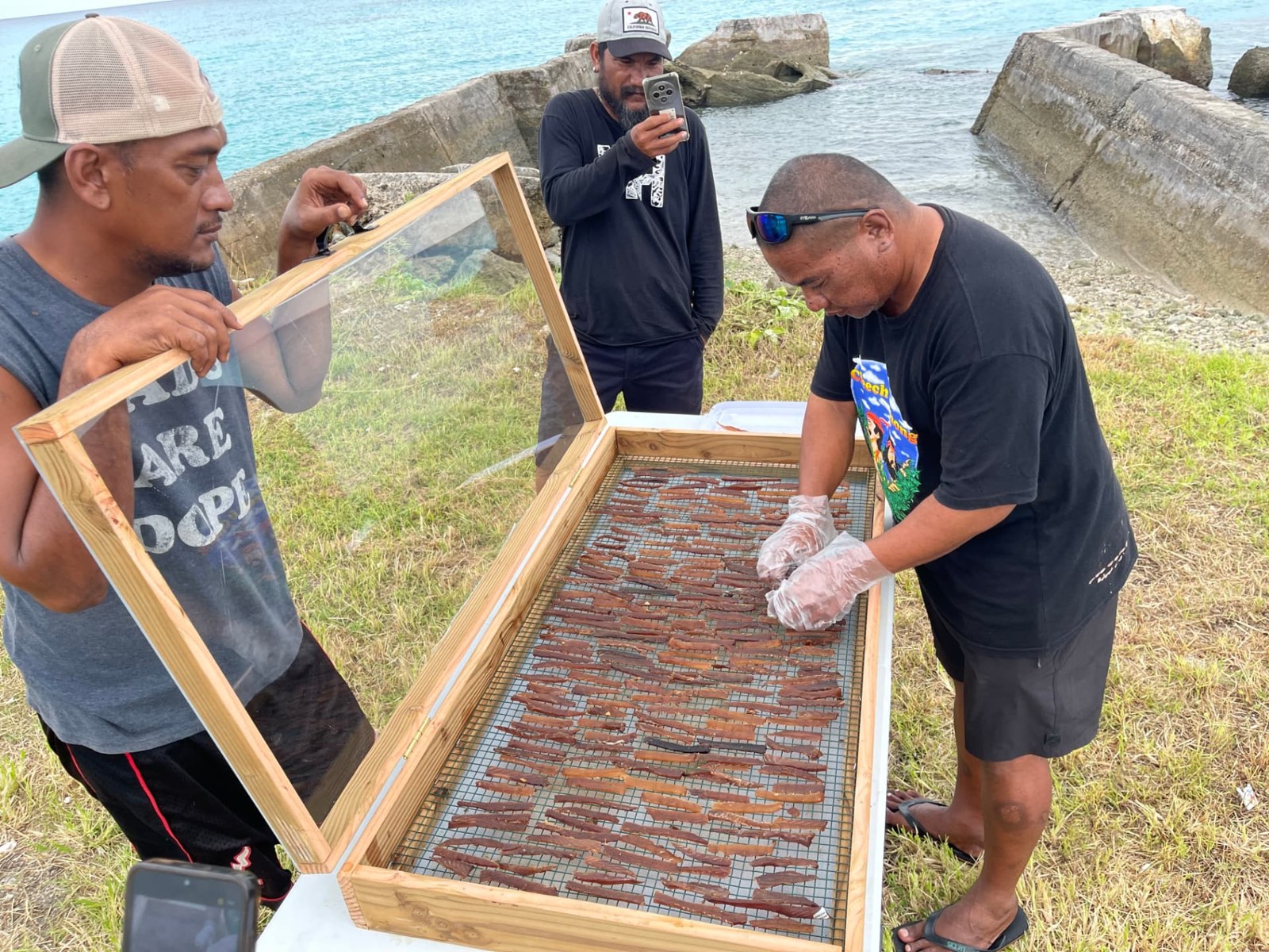 People preparing food in a wooden drying frame beside the ocean